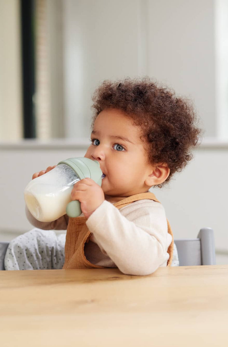 baby holding a feeding bottle filled with milk